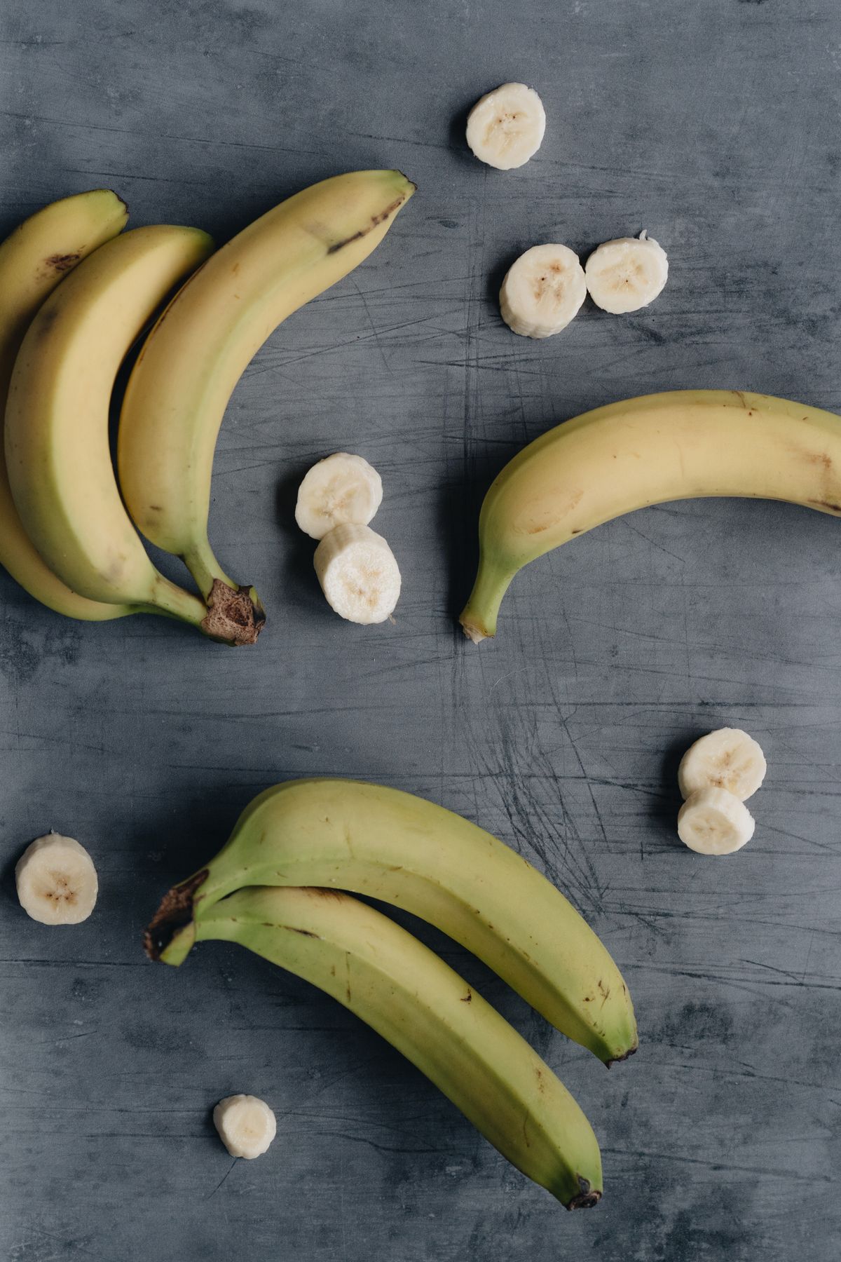 Whole bananas and banana slices on a grey surface
