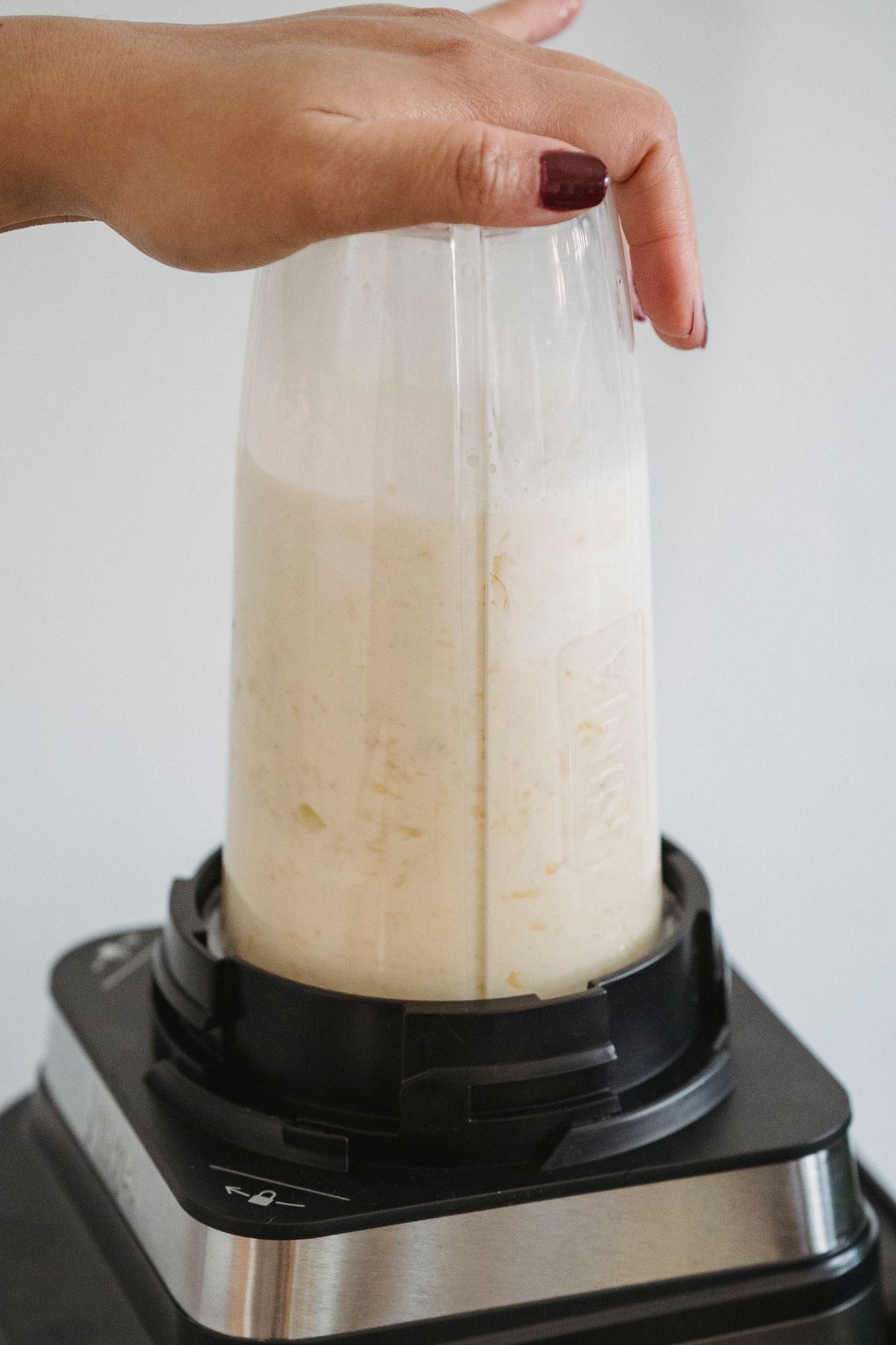 A hand operating a blender filled with a pale smoothie