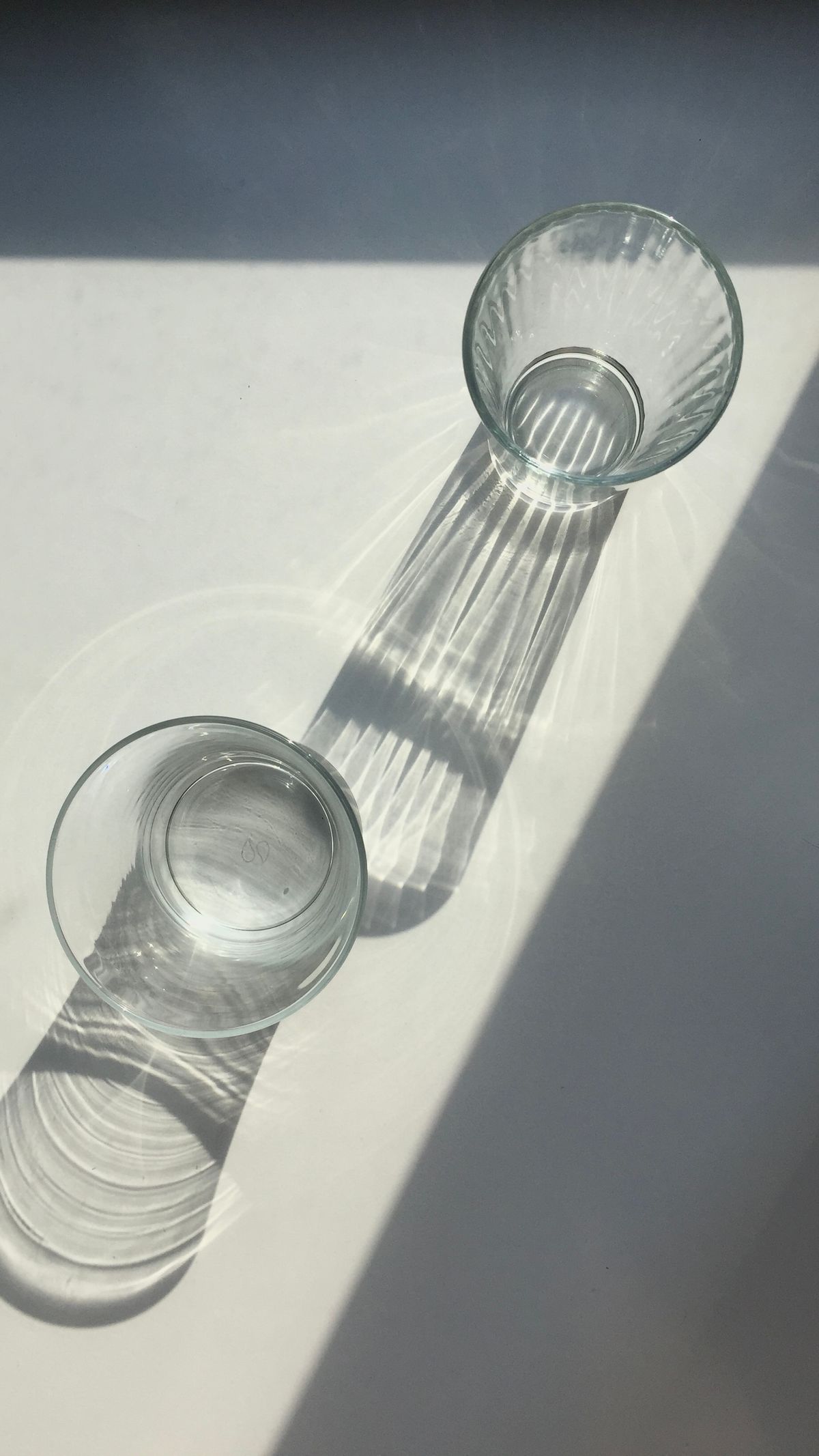 Empty clear glasses casting shadows on a white surface