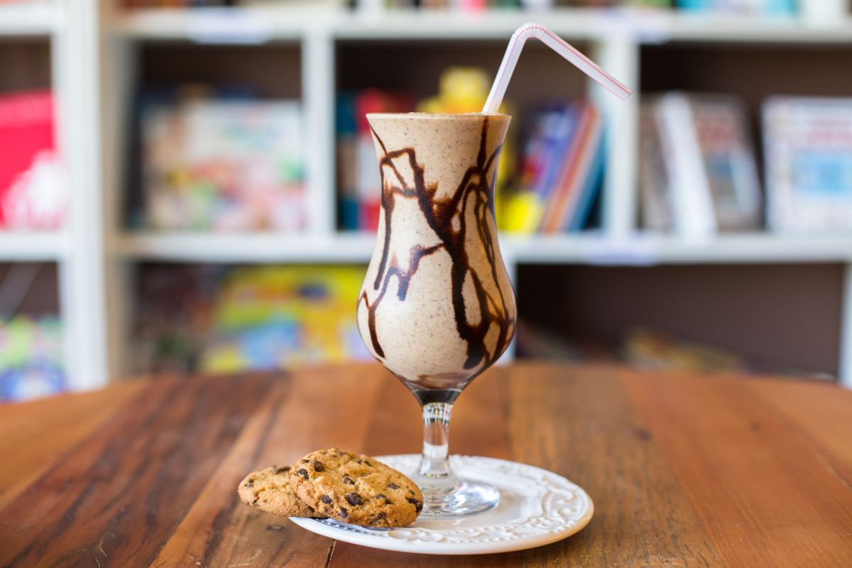 Chocolate frappe with a straw beside chocolate chip cookies
