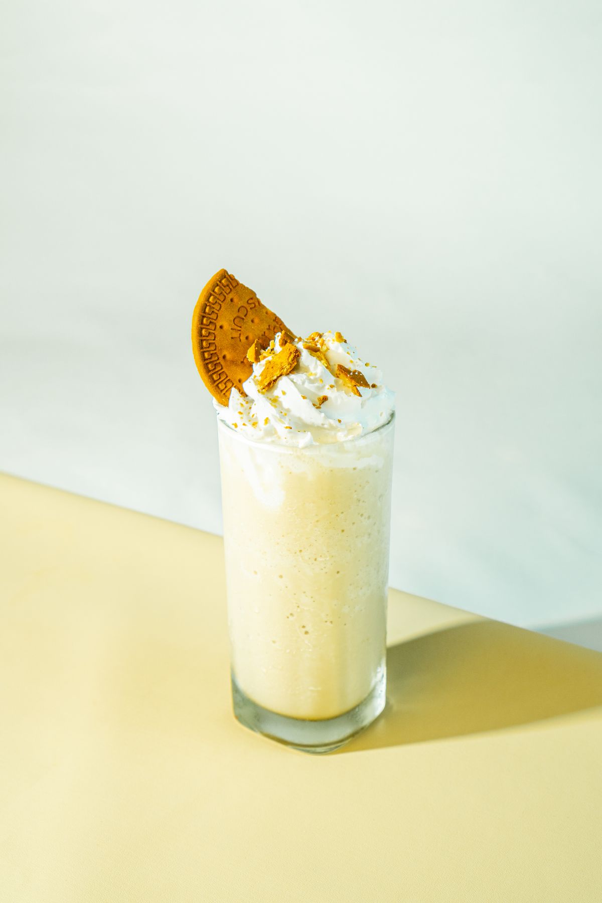 Vanilla milkshake topped with whipped cream and a biscuit